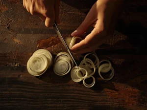 A top-down shot of a chef's hands using a sharp knife to separate sliced onions into individual rings on a dark wooden cutting board, the first step to making homemade crispy onion rings