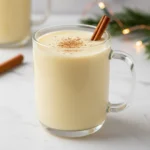 A glass mug of thick, creamy homemade eggnog, garnished with a cinnamon stick and nutmeg, representing the finished Homemade Eggnog Recipe for Christmas.