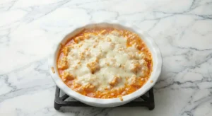 A white pie plate filled with the buffalo chicken dip recipe, fresh from the oven, showing the melted, golden cheese top and the filling bubbling around the edges.