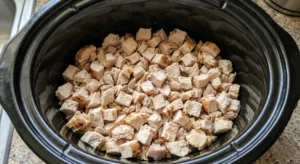 Chopped, cooked chicken cubes spread in an even layer at the bottom of a slow cooker insert, ready to be layered for crockpot buffalo chicken dip.