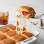 A spatula lifting a cheesy pull apart pizza slider from the pan, creating a long cheese pull, demonstrating the final Pull Apart Pizza Sliders Recipe.