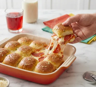 A spatula lifting a cheesy pull apart pizza slider from the pan, creating a long cheese pull, demonstrating the final Pull Apart Pizza Sliders Recipe.