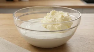 Bakery style carrot cake frosting step showing pale fluffy whipped butter added to a bowl of smooth cold cream cheese on an oak table.