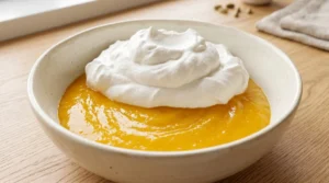 Homemade mango ice cream folding step showing fluffy white whipped cream resting on top of vibrant orange mango puree in a ceramic bowl.