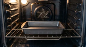 New york cheesecake water bath setup showing an empty dark metal baking pan placed on the lowest wire rack inside an oven.