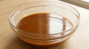 Homemade carrot cake wet ingredients showing a smooth, rich brown mixture in a clear glass bowl on a light oak wood table.