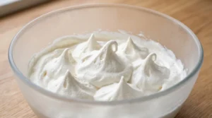 Creamy mango ice cream base showing cold whipped cream with perfect soft-to-medium peaks inside a clear glass bowl.