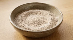 Easy carrot cake recipe dry ingredients step showing a rustic bowl filled with evenly whisked flour, baking powder, baking soda, salt, and toasted spices on a light oak table.