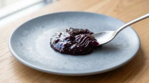 To show the best old fashioned blackberry jam recipe, a silver spoon pushes deep purple fruit on a chilled grey plate. It rests on a light oak wood table in bright natural window light. We bend the strictly zero utensils rule here to clearly show this vital step. Checking for a wrinkle on a cold plate is the quick and easy way to know if your sweet batch has reached the perfect gel point today!
